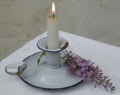 a white candle sitting on top of a saucer next to a plate with purple flowers