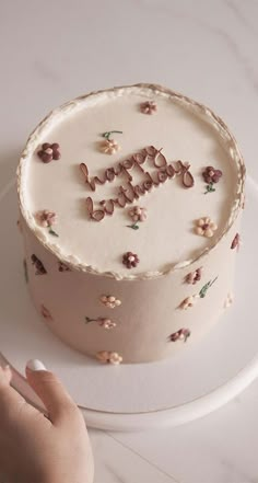 a hand is holding a cake with the word happy on it and flowers all over it