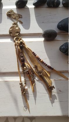 an assortment of necklaces hanging on a white wooden wall next to rocks and stones