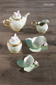 four pieces of porcelain tea set with butterfly decorations on the top and bottom, sitting on a wooden surface