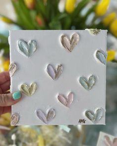 a hand holding up a card with hearts on it and some flowers in the background