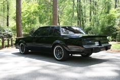 a black car is parked on the side of the road in front of some trees