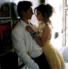 a man and woman standing next to each other in front of a wall with posters on it