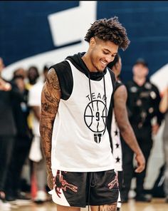 a young man standing on top of a basketball court wearing black and white clothing with tattoos