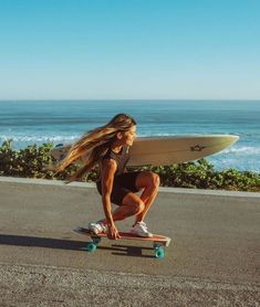 a woman riding a skateboard down the side of a road next to the ocean