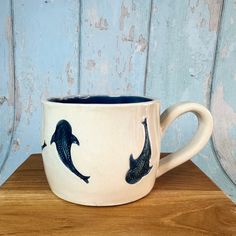 a coffee cup with two dolphins painted on the outside and inside, sitting on a wooden table