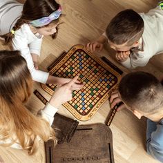 four people sitting at a table playing a board game with pieces on the floor, looking down