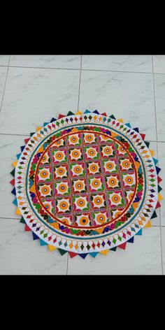 a colorful round rug on the floor in front of a white tile wall with multicolored designs