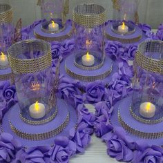 there are many candles in glass vases with purple flowers on the bottom and gold trim around them