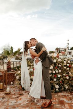 a bride and groom kissing in front of flowers at their wedding ceremony on the roof of a building