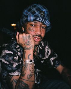 a young man with tattoos on his arm and hand is posing for the camera while wearing a hat