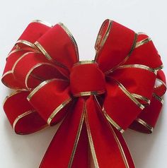 a red bow with gold stripes on it sitting on a white surface, ready to be used as an ornament