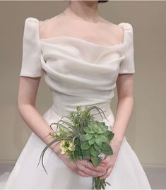 a woman in a white wedding dress holding a bouquet of greenery and succulents