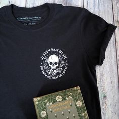 a black t - shirt with a green book and skull on it sitting next to a pair of scissors