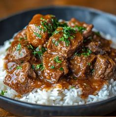 a black bowl filled with rice and meat covered in gravy on top of a wooden table