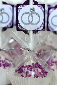 purple and white cupcakes with wedding rings on them are displayed in clear wrappers