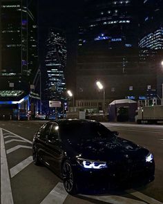 a black car is parked on the street in front of some tall buildings at night