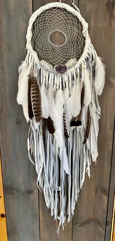 a white and brown dream catcher hanging on a wooden wall with feathers attached to it