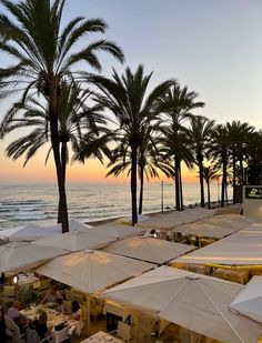 tables and umbrellas are set up on the beach for an outdoor dining event at sunset