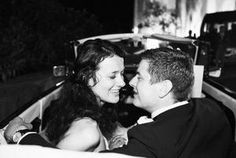 black and white photograph of a couple in a convertible car smiling at each other while the bride is holding her groom's hand