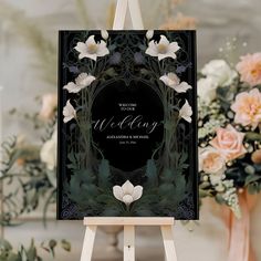 an easel with a wedding sign on it and flowers in vases behind it