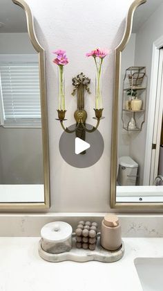 a bathroom sink with two mirrors and flowers on the wall next to it's mirror