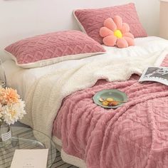 a bed with pink comforter and pillows on it next to a vase filled with flowers