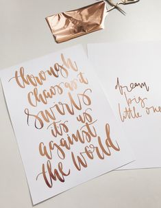 three different types of calligraphy on white paper with copper foil and scissors next to them