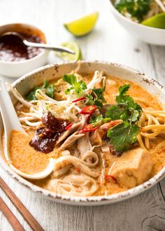 a bowl filled with noodles, meat and veggies next to chopsticks