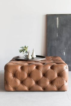 a brown leather ottoman sitting in front of a painting