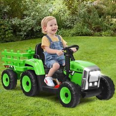 a young boy riding on the back of a green toy tractor in a grassy field