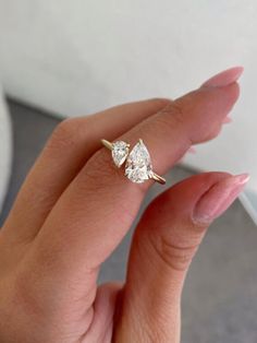 a woman's hand holding a ring with two pear shaped diamonds on top of it