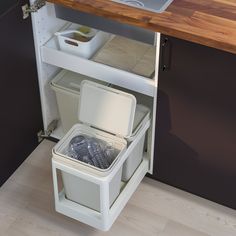 an open cabinet in the corner of a kitchen with a sink and trash can underneath it