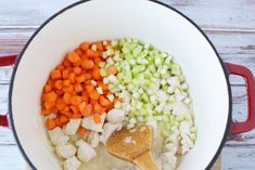 the vegetables are being cooked in the pot on the wooden table, including carrots and celery