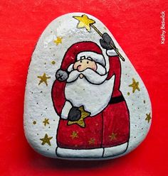 a painted rock with a santa clause holding a star and pointing to the sky on it