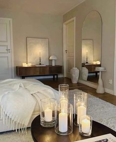 candles are placed on a table in front of a bed with white sheets and pillows