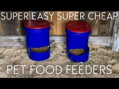 two blue plastic containers with red lids sitting on top of sand next to a wooden fence