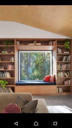 a living room with bookshelves and a window in the middle that has a view of trees