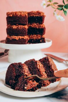 a white plate topped with chocolate cake next to a stack of brownies on top of a table