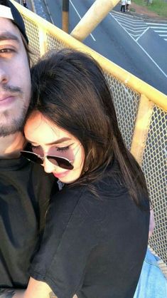 a man and woman sitting next to each other in front of a fence with an empty street behind them