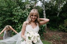 a woman in a wedding dress holding a bouquet and posing for the camera with her arms behind her head