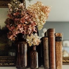 some books and vases are sitting on a shelf next to each other with flowers in them