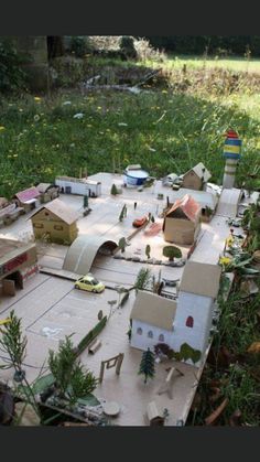 a model train set in the middle of a field with cars and buildings on it