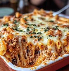 a casserole dish with meat, cheese and sauce in it on a wooden table