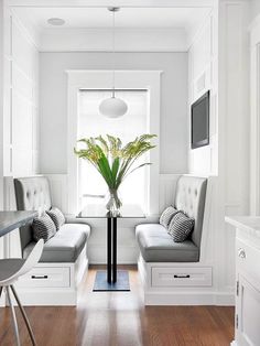 a kitchen with white walls and wooden floors, along with two gray benches on either side of the window sill