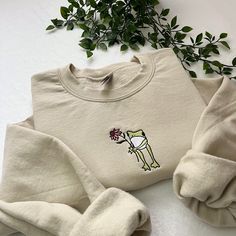 ✿ Flower Frog Embroidered Sweatshirt 🐸🌸 - ✿ Frog with flower embroidered on a unisex sweatshirt! an amazing gift idea!  - ✿ This design can be done on different coloured sweatshirts and with different coloured thread, as well as on totes, t-shirts and hoodies so please message me if you'd like to personalise it!  - ✿ Please look at the last slide for the size guide! I do not accept returns if you pick the wrong size, so please make sure you choose the correct one!  - ✿ I have lots of other ite Embroidered Clothes Ideas, Hoodie Embroidery Ideas, Embroidery Sweatshirt Ideas, Frog With Flower, Sweatshirts Ideas, Embroidery Sweaters, Embroidered Frog, Frog Embroidery, Frog Sweatshirt