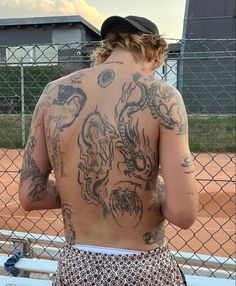 a woman with tattoos on her back standing in front of a fence