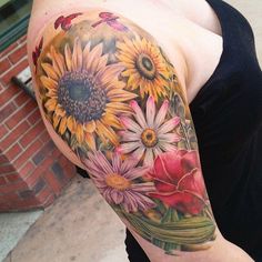 a woman's arm with sunflowers and flowers on the left side of her body