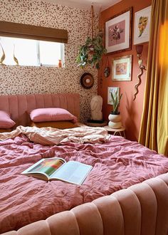 a bed with pink sheets and pillows in a bedroom next to a window filled with plants