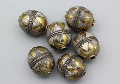 five gold and silver beads on a gray surface with white dots in the middle one bead has an intricate design